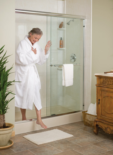 Middle-aged woman wearing a white bathrobe is stepping out of the shower onto a mat