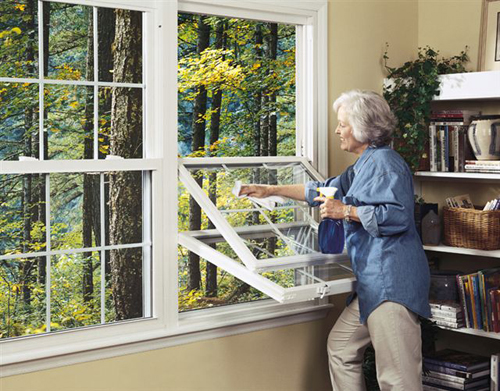 Middle-aged woman with gray hair is cleaning double-hung windows from the inside of a home.